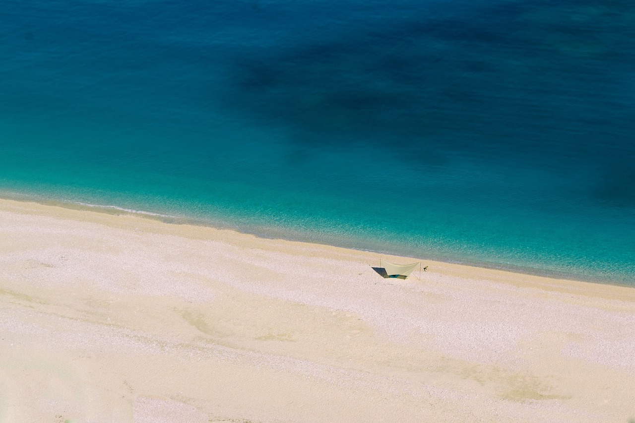 Spiaggia nascosta con sabbia rosa, circondata da scogli e acqua cristallina.