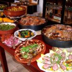 Immagine di un borgo italiano con piatti tipici della cucina regionale su un tavolo all'aperto.