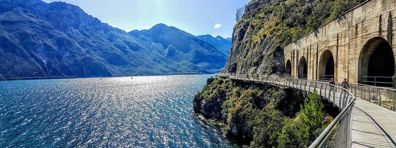 Sentiero panoramico tra due laghi alpini, circondato da montagne e vegetazione lussureggiante.